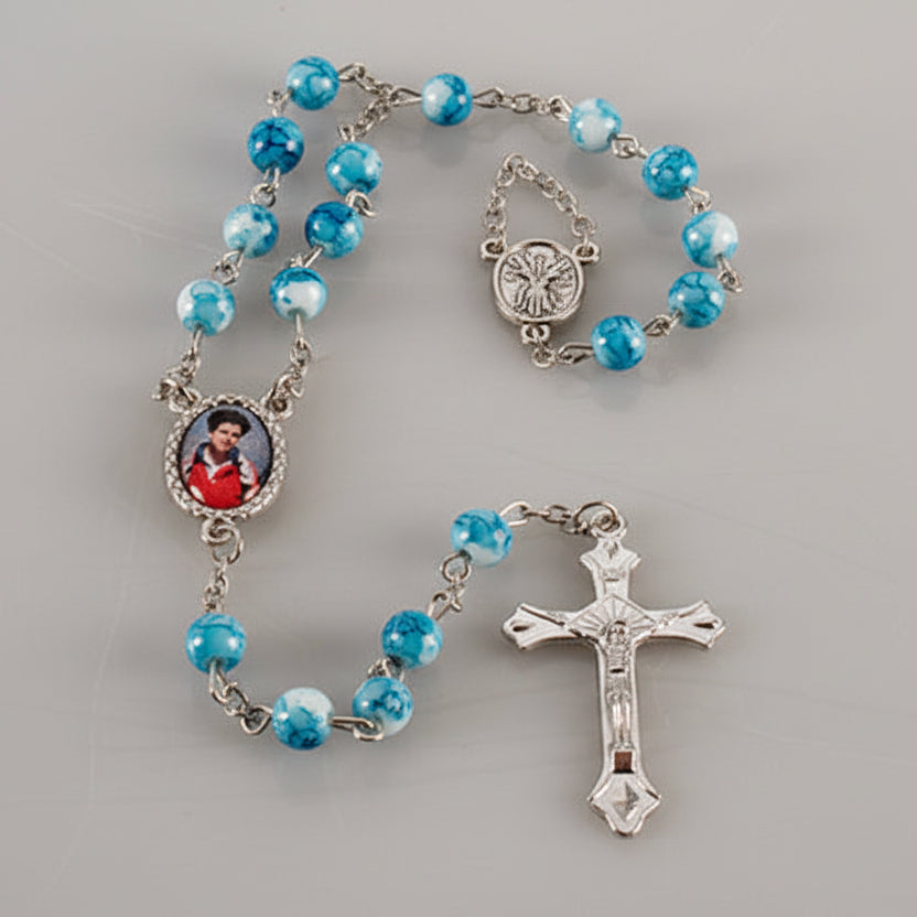 Blue rosary with silver cross and images of a person on gray background