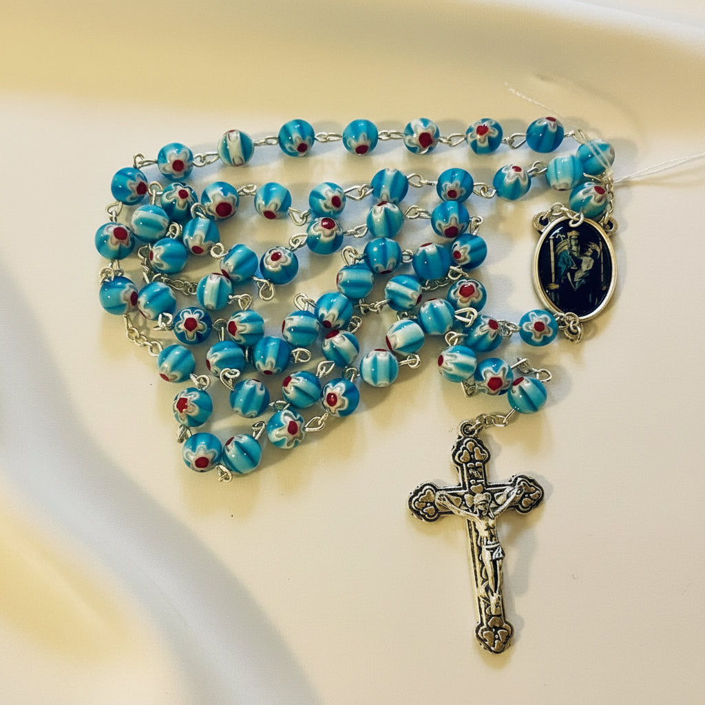 A rosary with blue glass beads featuring floral patterns, a silver-colored cross, and a medallion with an image in the center.