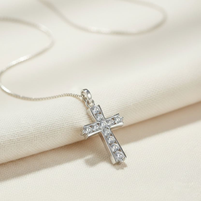 Silver cross pendant necklace with clear stones on a beige fabric background