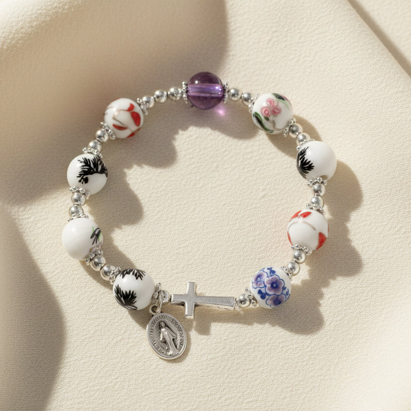 A glass bracelet with cross and medal charms, displayed on a card with the brand name CBC.