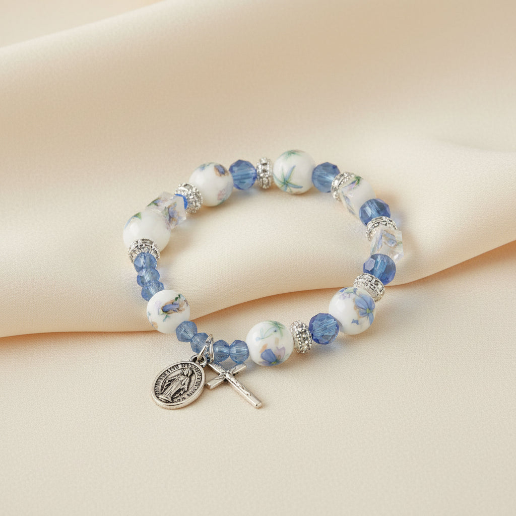A light blue bracelet with a mix of glass and ceramic beads featuring floral designs, a metal crucifix, and a Miraculous Medal.
