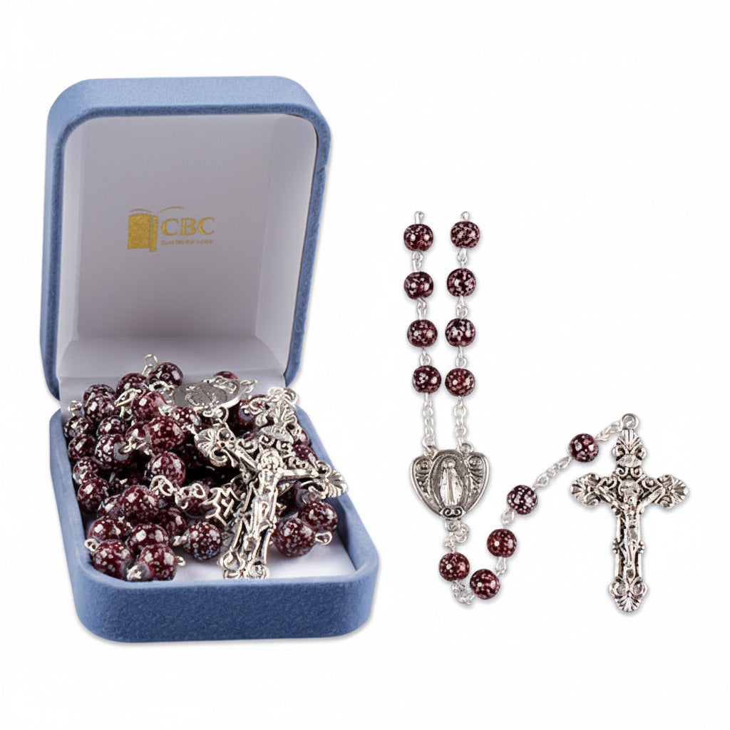A blue velvet box containing a glass rosary with amethyst marble effect beads and metal components, displayed alongside an image of the rosary outside the box.