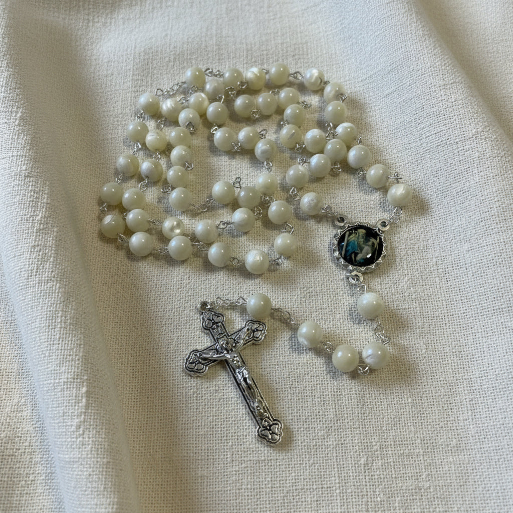 Rosary with white beads and silver cross on a light background