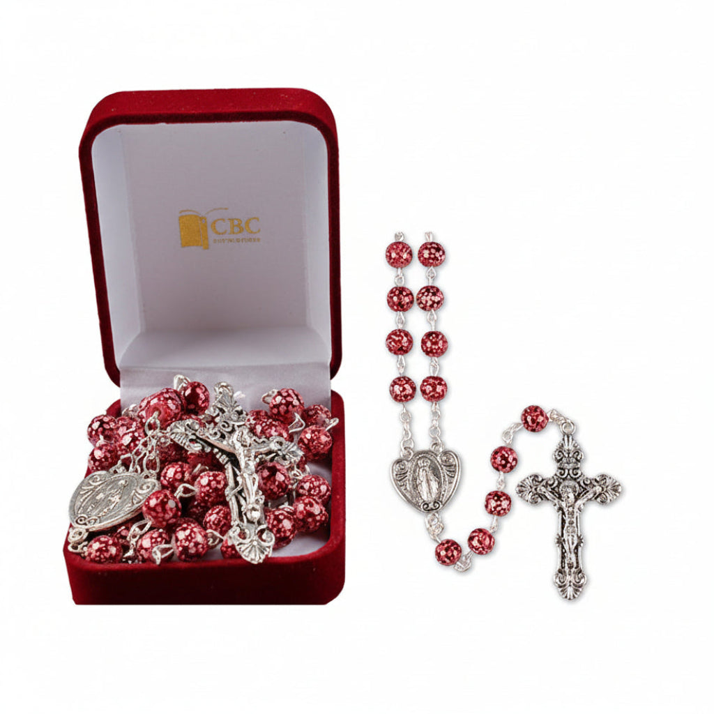 A dark red two-tone glass rosary displayed alongside its packaging, which includes a silver metal cross and Our Fathers Miraculous metal junction.