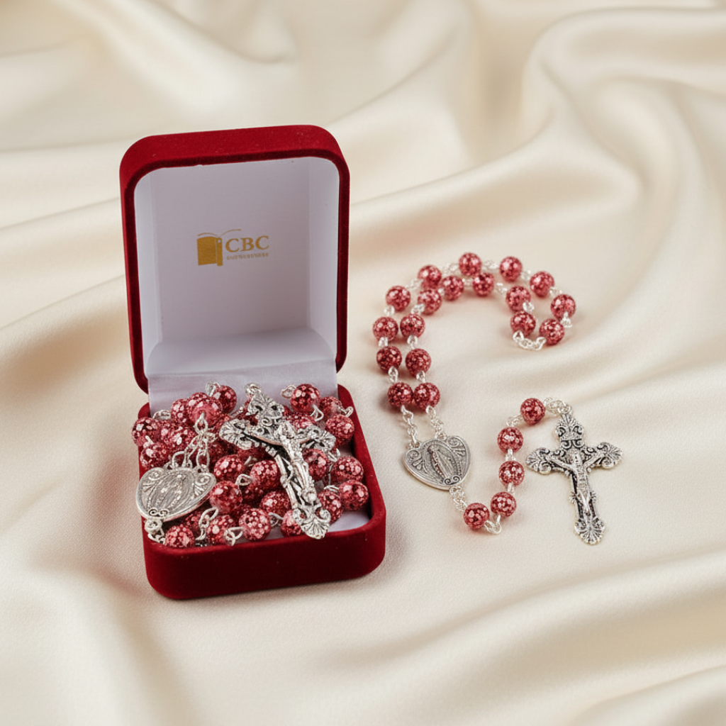 Pink rosary with silver crucifixes in a red velvet box on a beige fabric background