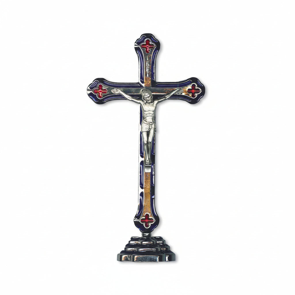 A polished metal finish standing crucifix with blue enamel inlay, featuring an image of Jesus on the cross with a red background and decorative elements around it.