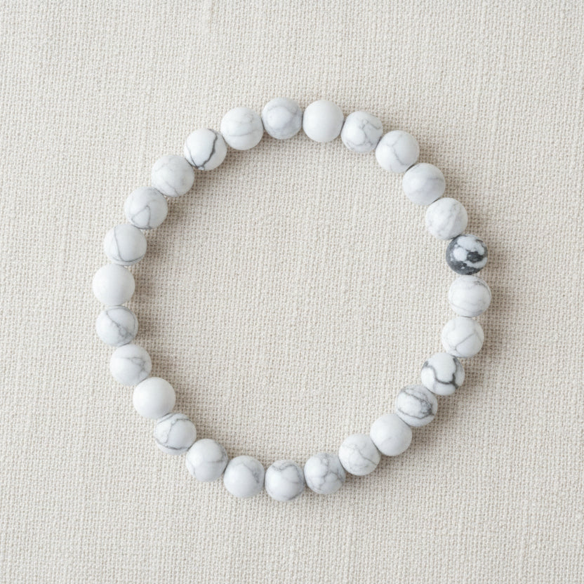White beaded bracelet on a 'Power Bracelets' card with text on a wooden surface