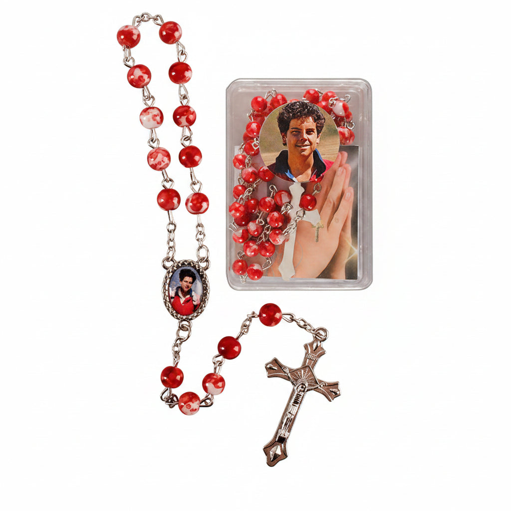 A red and silver rosary with a crucifix and an oval medallion, shown alongside its clear plastic packaging featuring a printed photo of a man.
