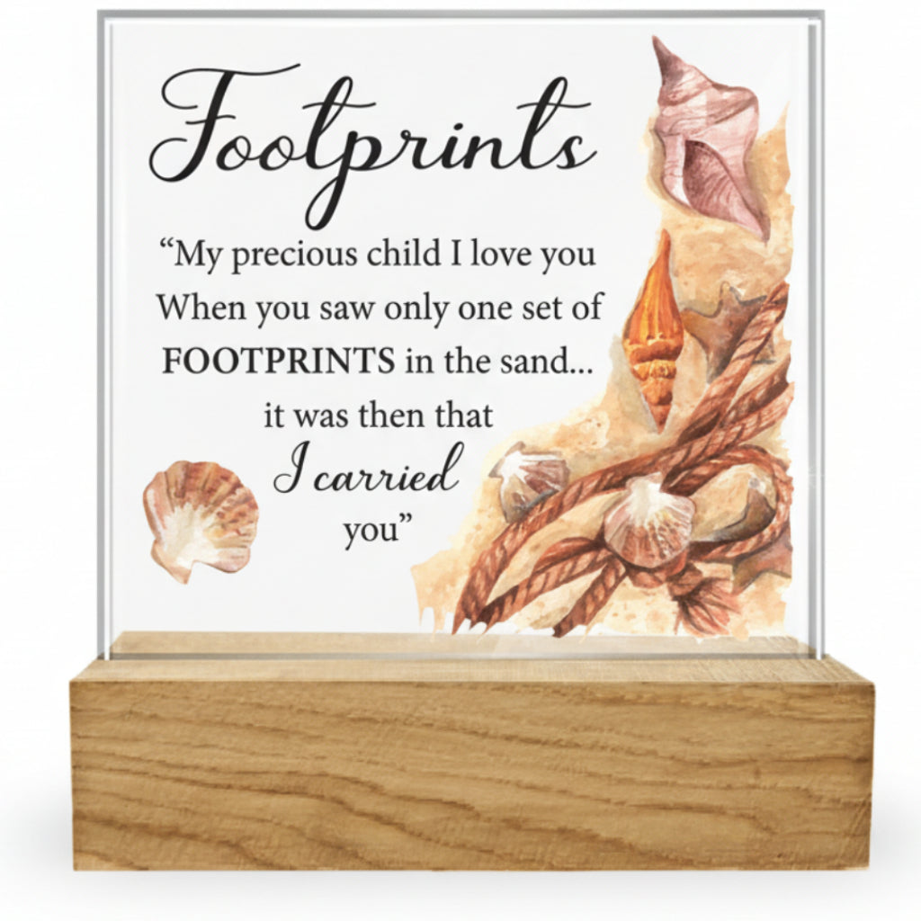 A glass plaque with bevelled edges featuring an artistic representation of footprints in the sand, alongside a quote. It is mounted on a wooden base.