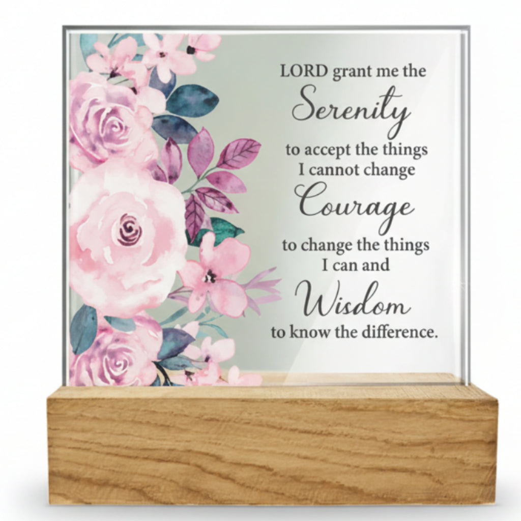 A glass plaque with bevelled edges featuring floral designs and the Serenity Prayer, placed on a wooden base.