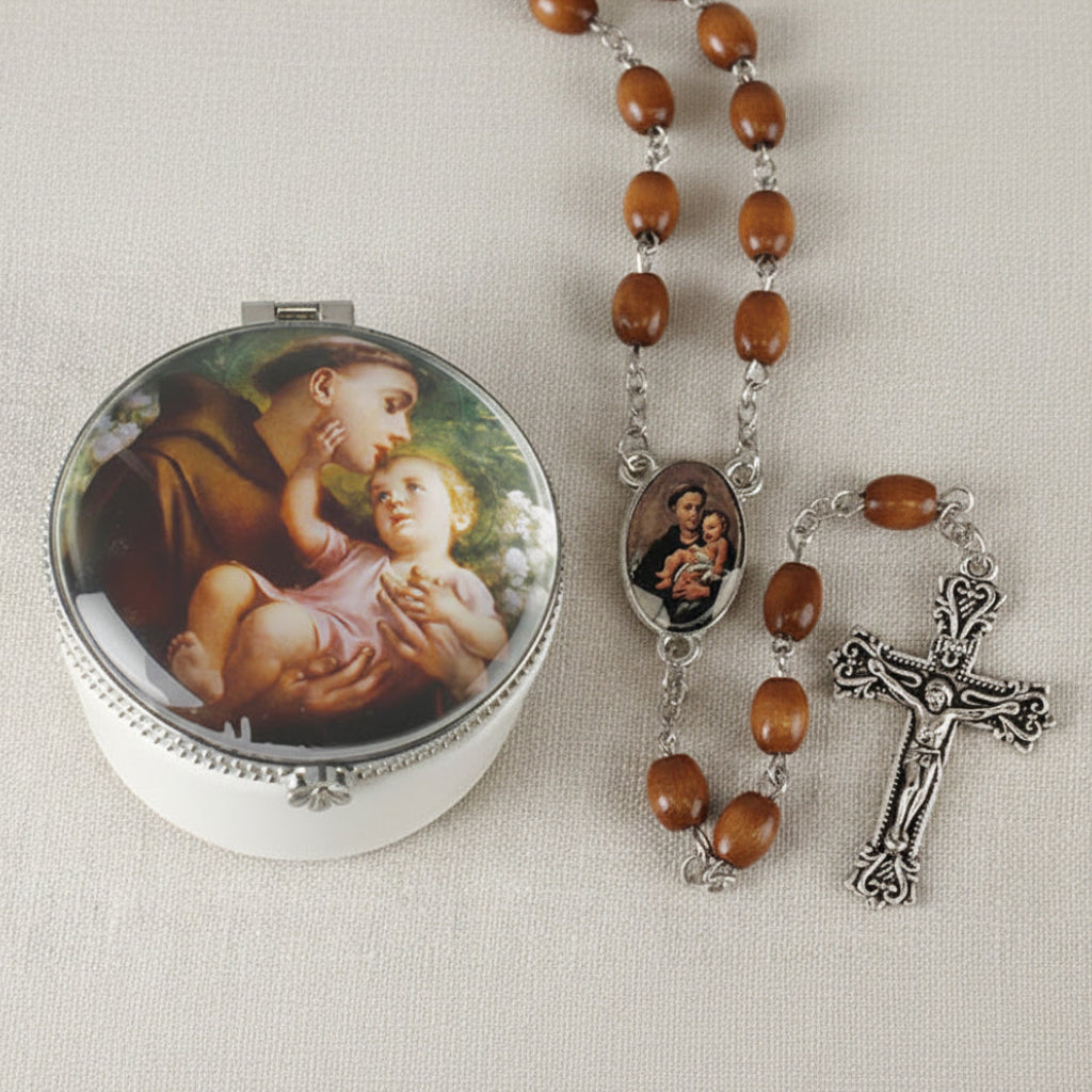 A brown wood rosary with a silver metal cross and a porcelain box with a picture of St. Anthony holding a child.