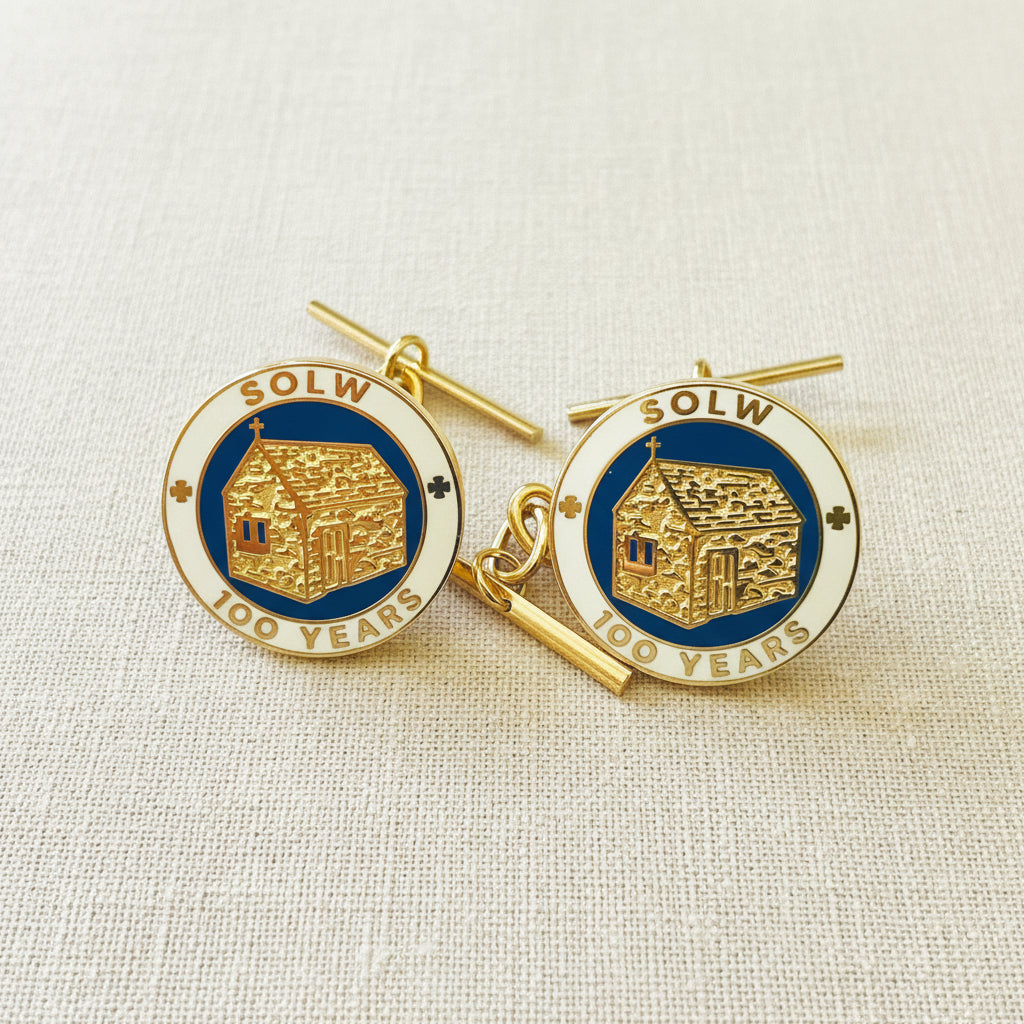 Two gold and blue enamel pins with a building illustration and '100 Years' text on a white background.