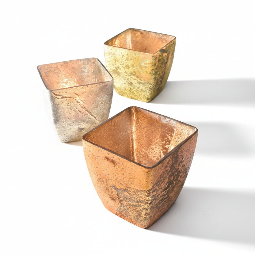 Three square, textured glass candle holders on a gradient background