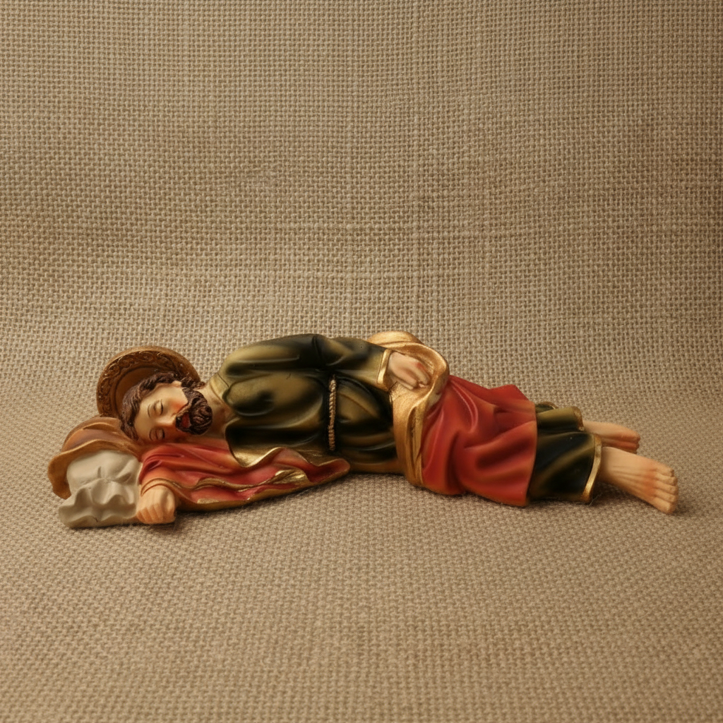 A resin sculpture of Sleeping St. Joseph, laying down, with detailed clothing and facial features, primarily in red, gold, and brown tones.